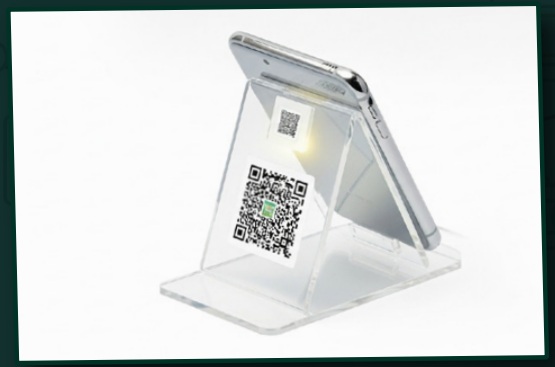 Clear acrylic counter stand holding a QR card beside a phone in the company profile