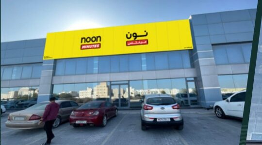 Shopfront with yellow bilingual signage and cars parked in front in the company profile — واجهة محل بلوحة صفراء باللغتين وسيارات متوقفة أمامها في بروفايل الشركة