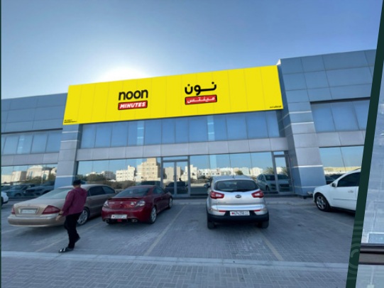 Shopfront with yellow bilingual signage and cars parked in front in the company profile — واجهة محل بلوحة صفراء باللغتين وسيارات متوقفة أمامها في بروفايل الشركة